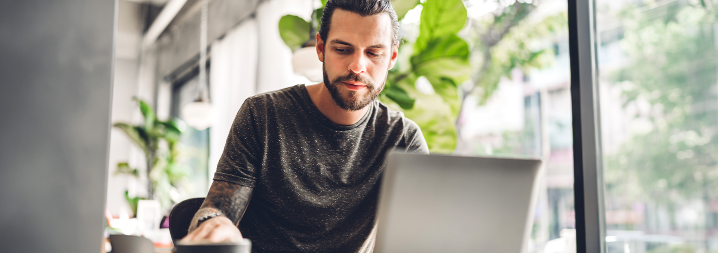 Junger Mann mit Kaffeetasse vor Laptop